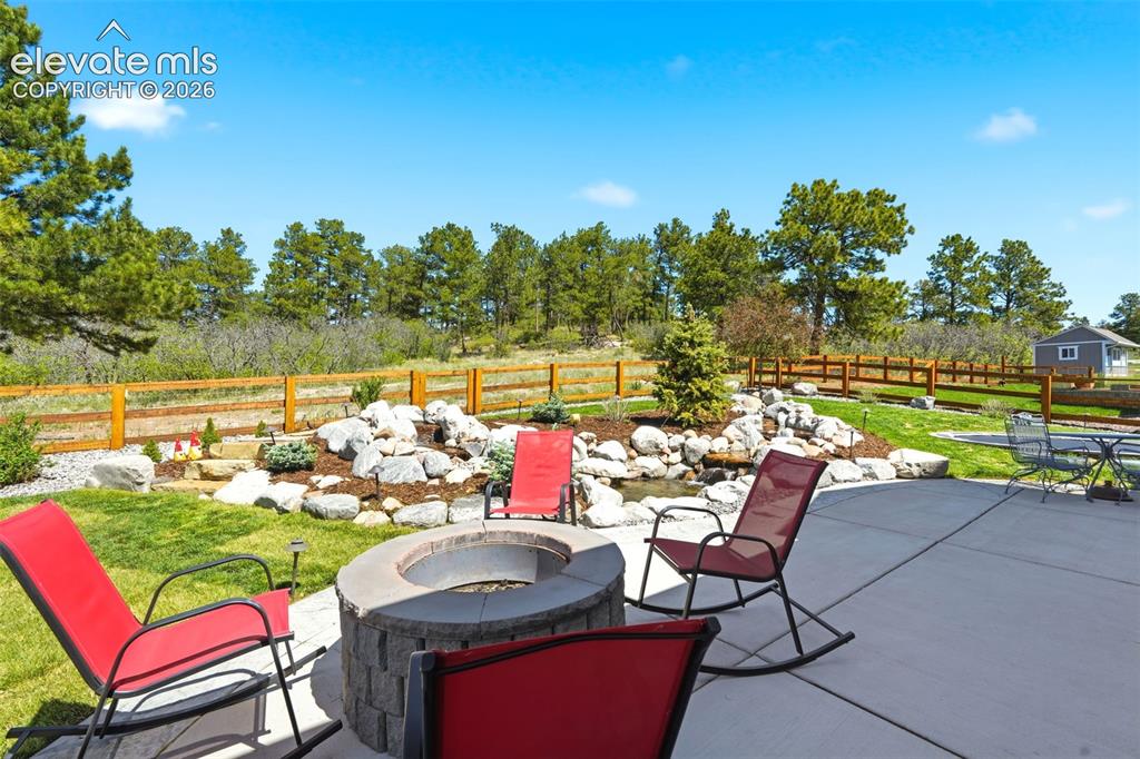 Image 36 of 44: Spacious patio featuring a built-in stone fire pit, extensive concrete hard