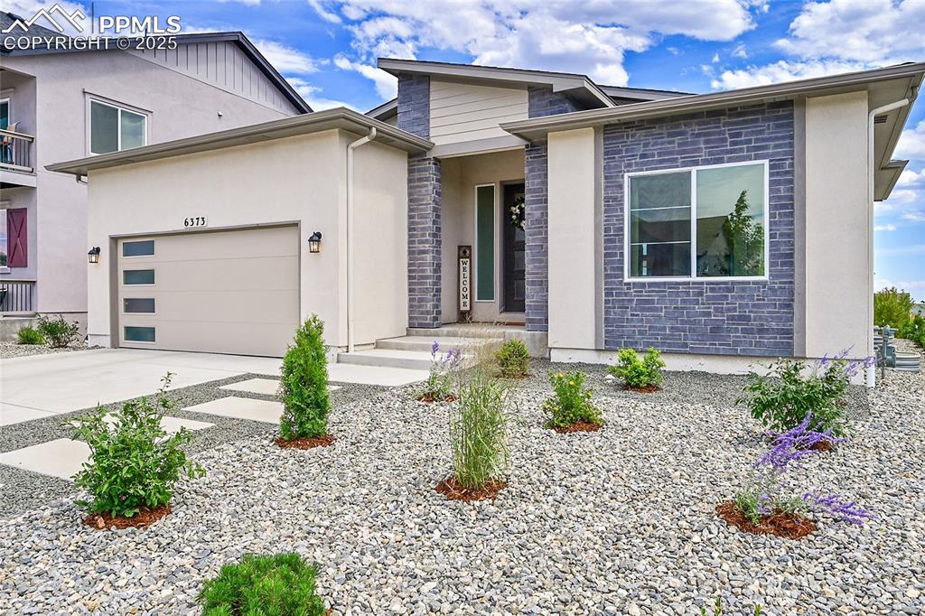 Caption: View of front facade with driveway, stone siding, an attached garage, and stucco siding