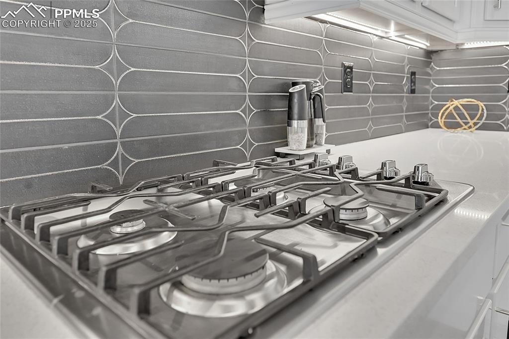 Image 10 of 44: Kitchen view of stainless steel gas stovetop and white cabinetry