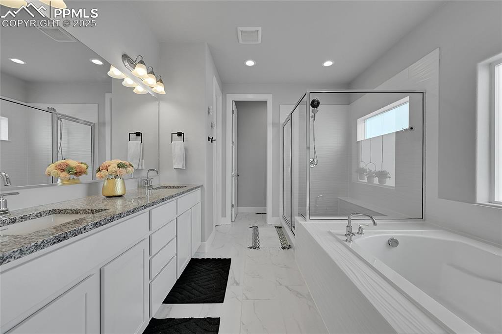 Image 19 of 44: Bathroom featuring marble look tile flooring, double vanity, a bath, a stal