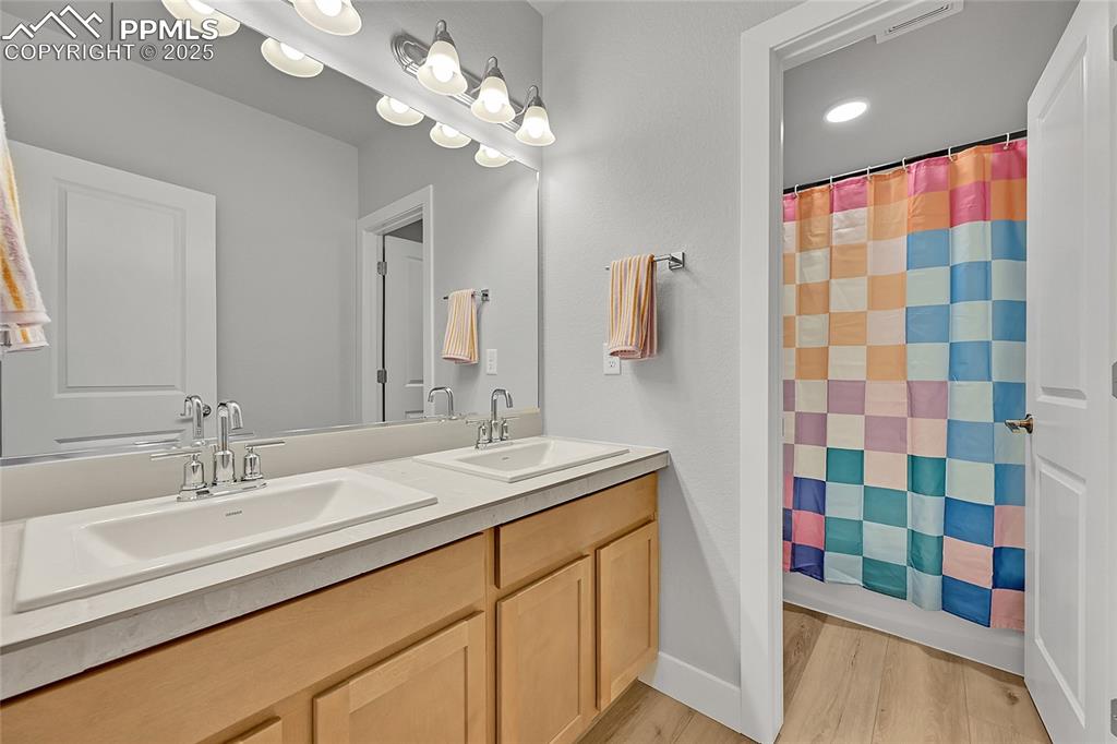 Image 31 of 44: Bathroom featuring wood finished floors, double vanity, and a shower with c