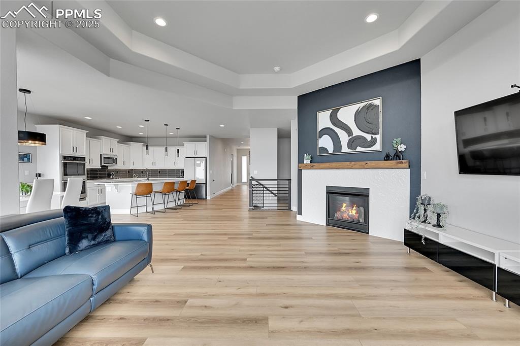 Image 7 of 44: Living area with a tray ceiling, recessed lighting, light wood-type floorin