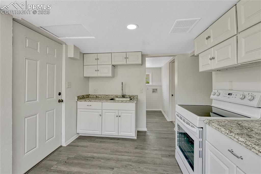Image 8 of 29: Kitchen with electric stove, white cabinets, light wood-style flooring, rec