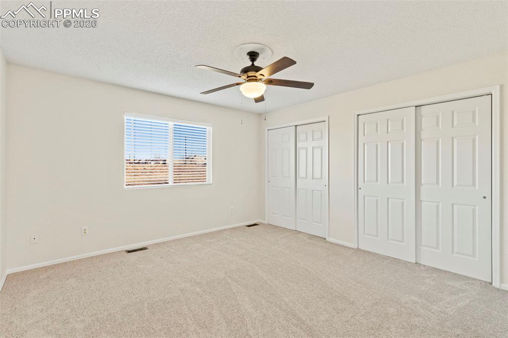 Image 16 of 26: Primary bedroom with two closets, a textured ceiling, light carpet, and a c