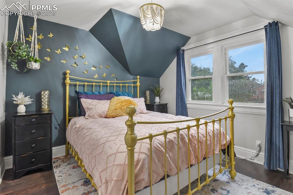 Image 23 of 36: Bedroom featuring dark wood-style floors, lofted ceiling, and a chandelier