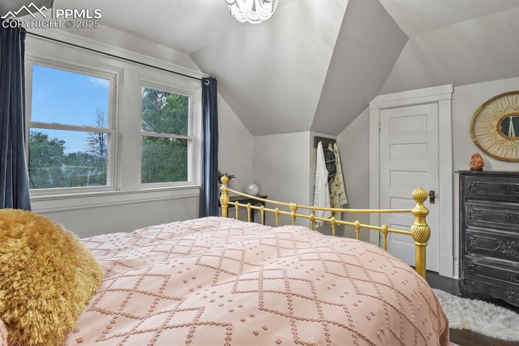 Image 24 of 36: Bedroom with lofted ceiling, a chandelier, and wood finished floors
