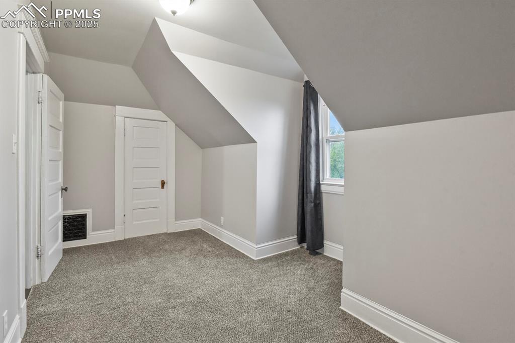 Image 28 of 36: Bonus room with vaulted ceiling and carpet flooring