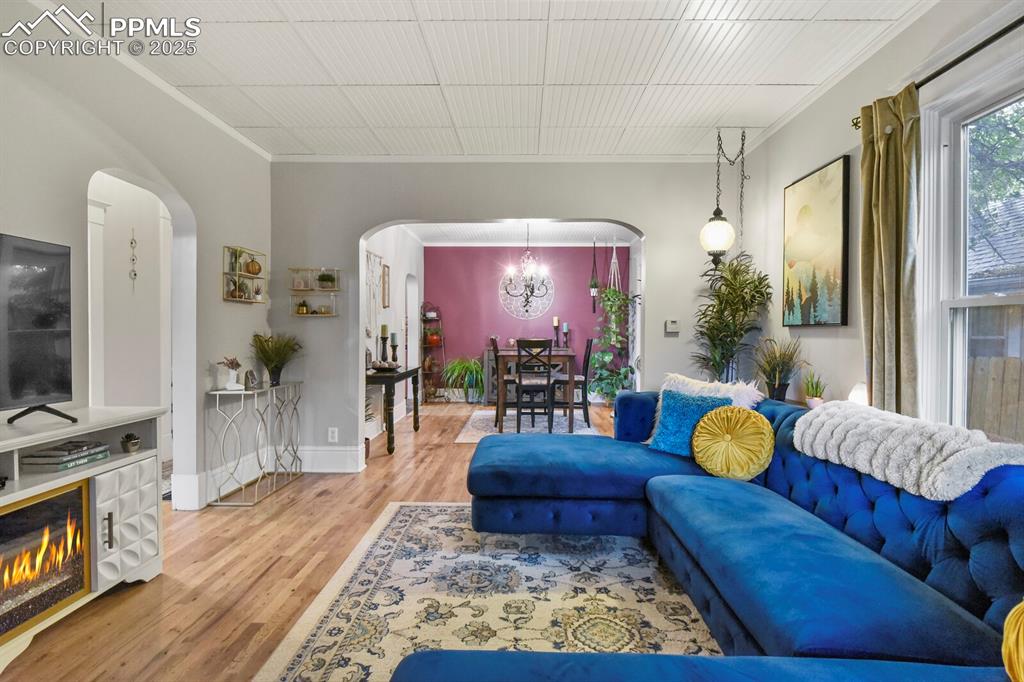 Image 9 of 36: Living area with arched walkways, light wood-style floors, crown molding, a