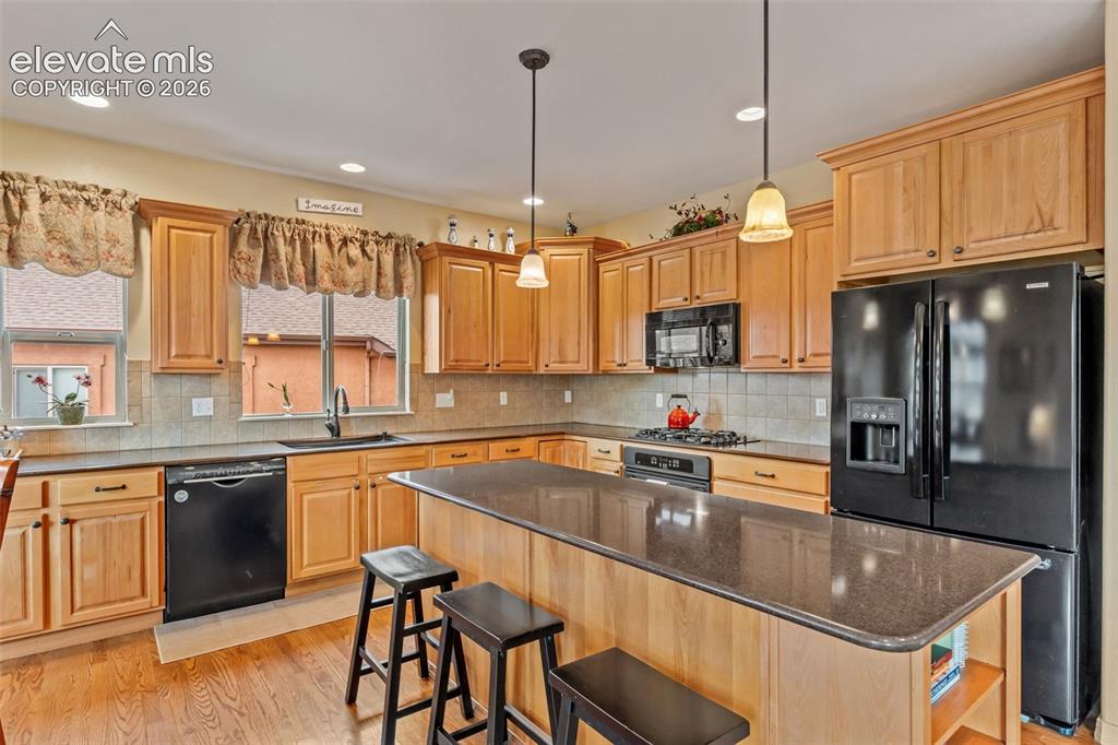 Image 16 of 50: Kitchen featuring wood-finish flooring, light wood cabinetry, black applian