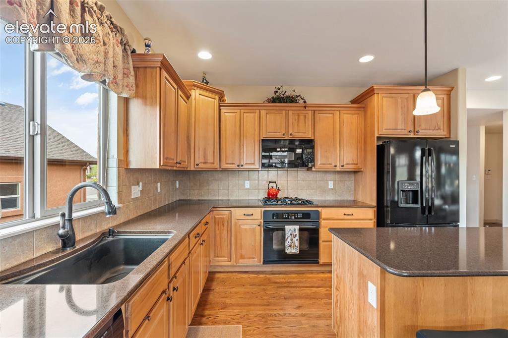 Image 17 of 50: Kitchen featuring light wood cabinetry, dark countertops, a large window ab