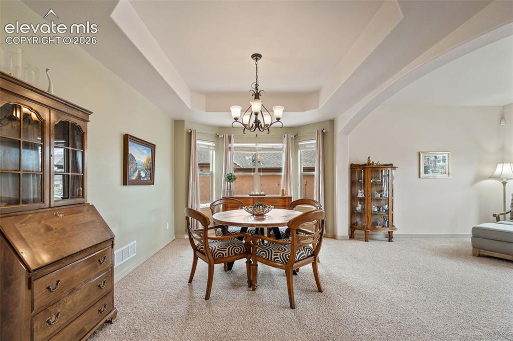 Image 9 of 50: Recessed ceiling with an elegant chandelier, bay window, and arched doorway