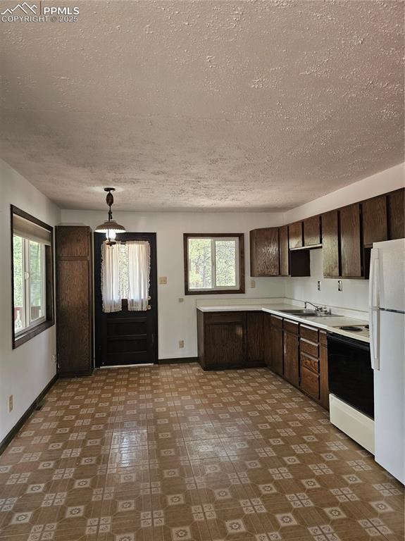 Image 3 of 13: Kitchen with light countertops, dark brown cabinetry, refrigerator, range, 