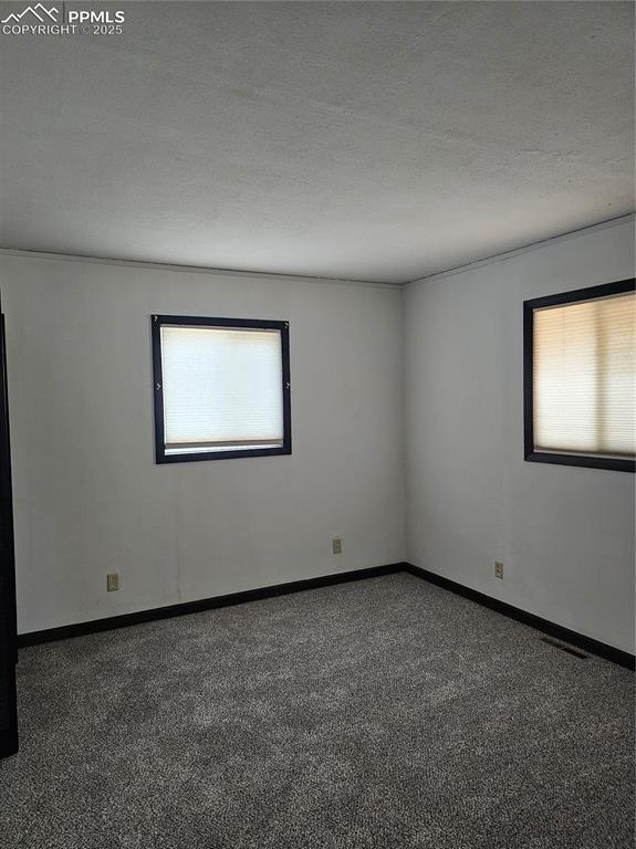 Image 6 of 13: Empty room featuring a textured ceiling, dark carpet, and healthy amount of