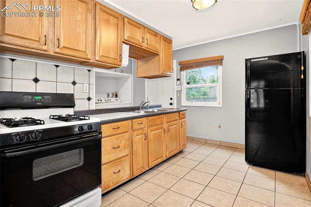 Image 2 of 12: Kitchen with range with gas stovetop, freestanding refrigerator, dark count