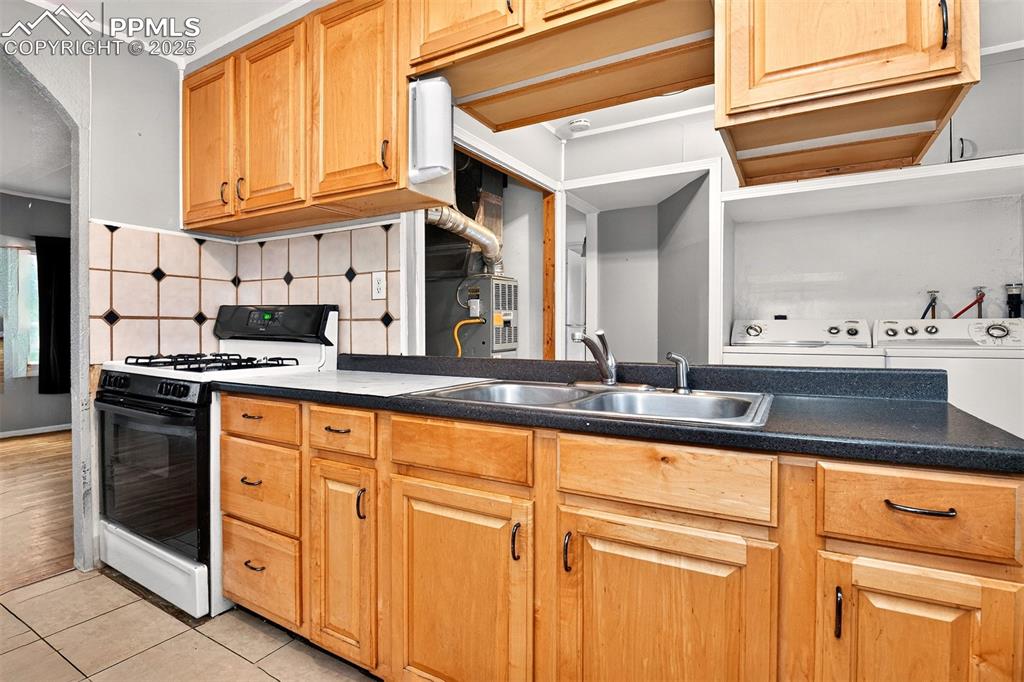 Image 3 of 12: Kitchen with washer and dryer, black gas range oven, light tile patterned f