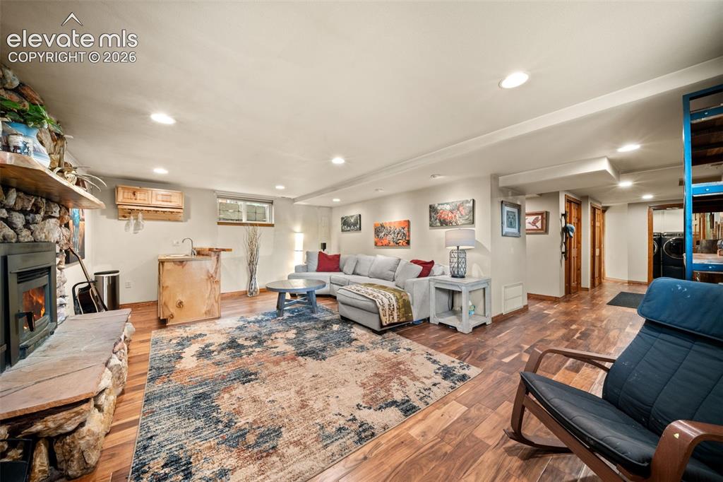 Image 22 of 45: Spacious lower-level living area with a cozy stone fireplace and wet bar.