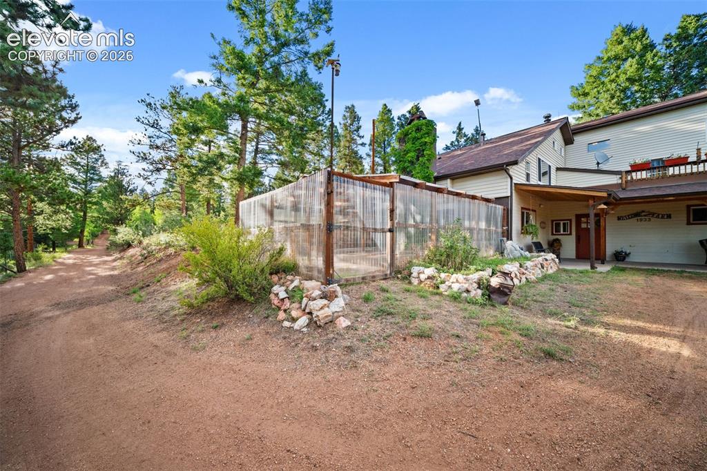 Image 33 of 45: Enclosed greenhouse and garden area surrounded by mature trees.