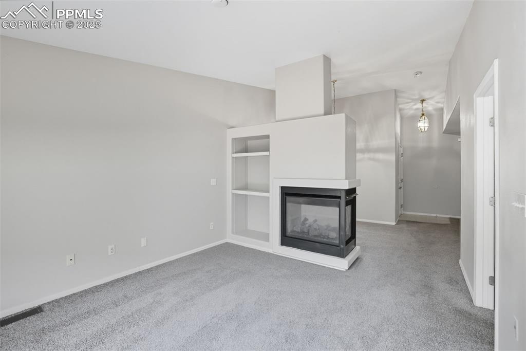 Image 18 of 47: Unfurnished living room featuring a multi sided fireplace and light carpet