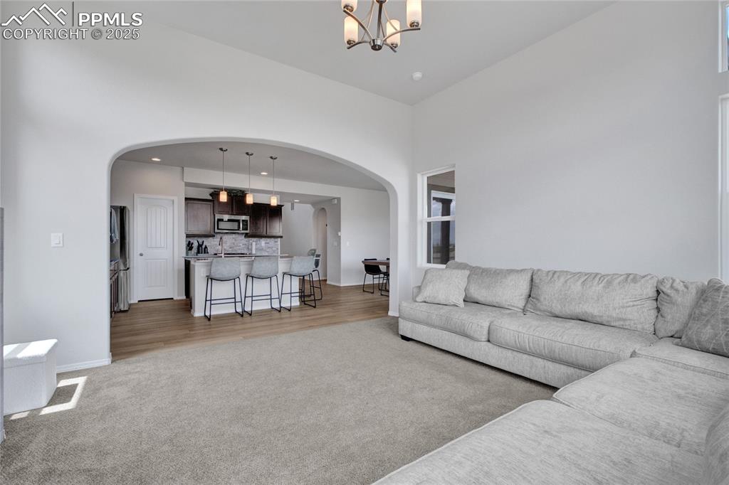 Image 13 of 41: Living area featuring light carpet, arched walkways, a chandelier, and a hi