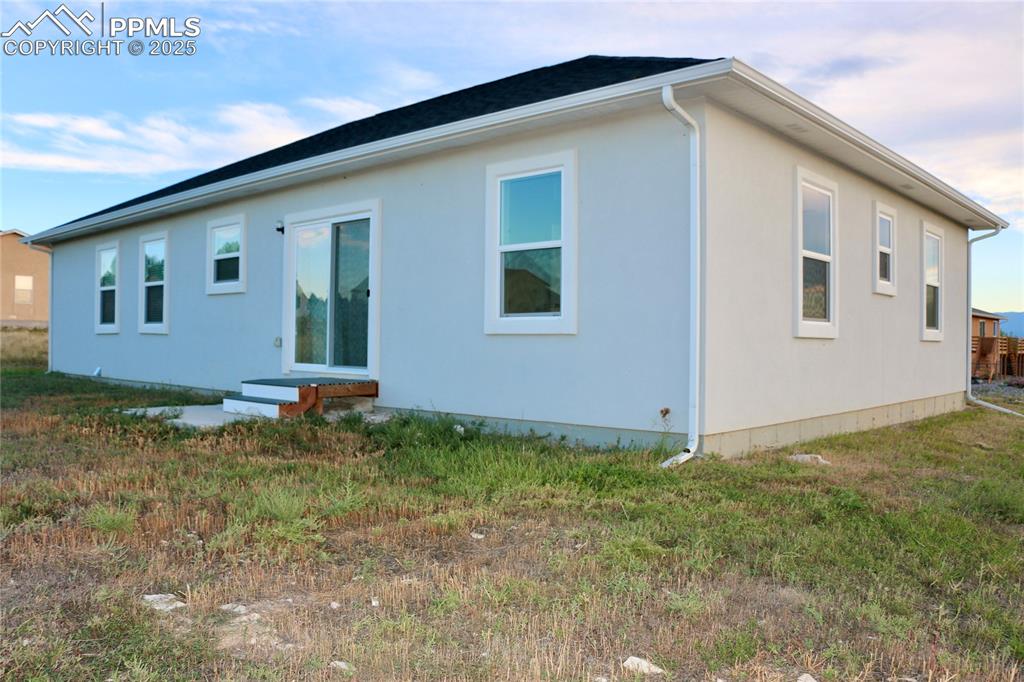 Image 29 of 30: Rear view of property with a lawn and stucco siding