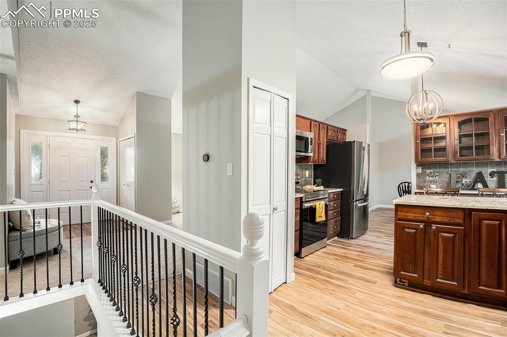 Image 16 of 34: Kitchen featuring lofted ceiling, a chandelier, backsplash, light wood-styl