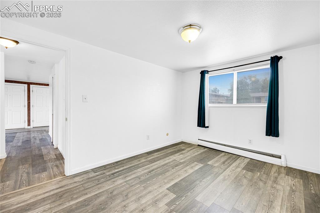 Image 16 of 29: Empty room with a baseboard heating unit and light wood-style floors