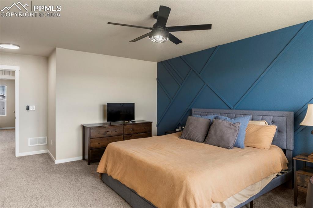 Image 10 of 32: Carpeted bedroom with a ceiling fan, an accent wall, and a decorative wall