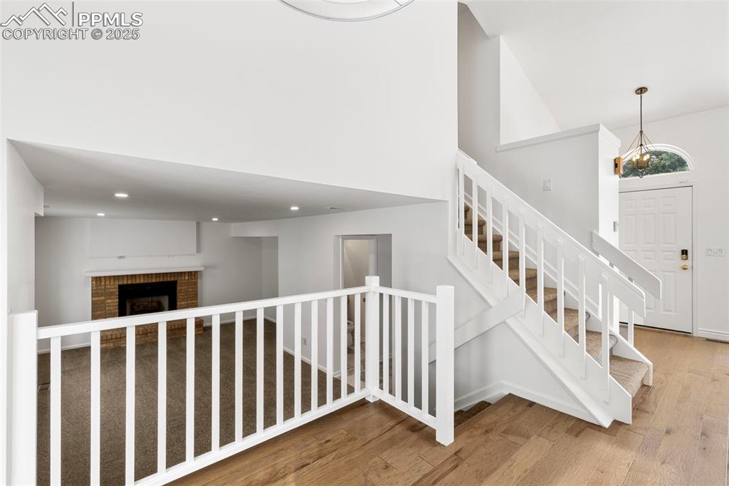 Image 11 of 27: Staircase with wood finished floors, a chandelier, a fireplace, recessed li