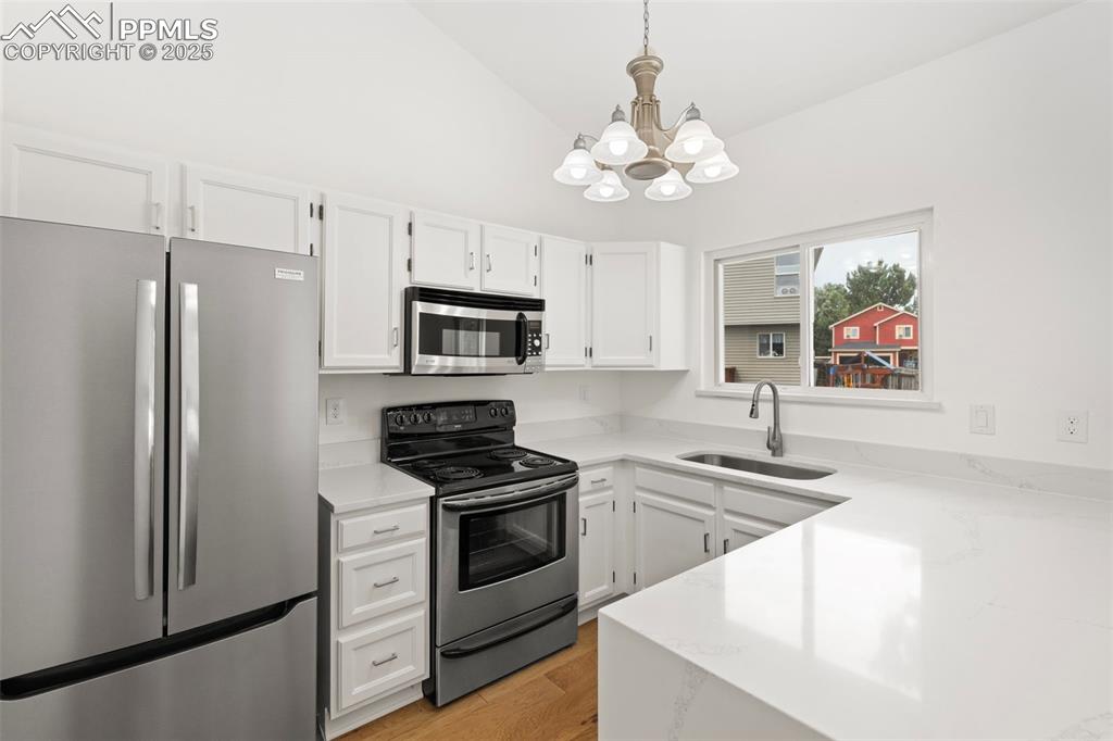 Image 8 of 27: Kitchen with stainless steel appliances, a chandelier, white cabinetry, lig