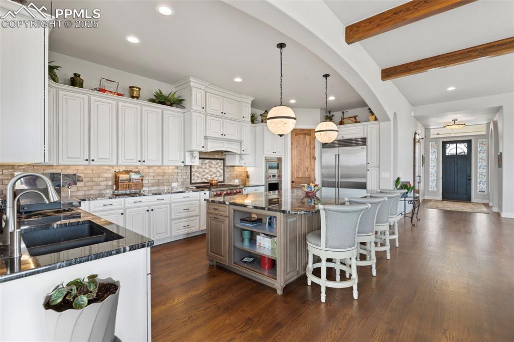 Image 20 of 50: Kitchen featuring beam ceiling, a breakfast bar, dark stone counters, decor