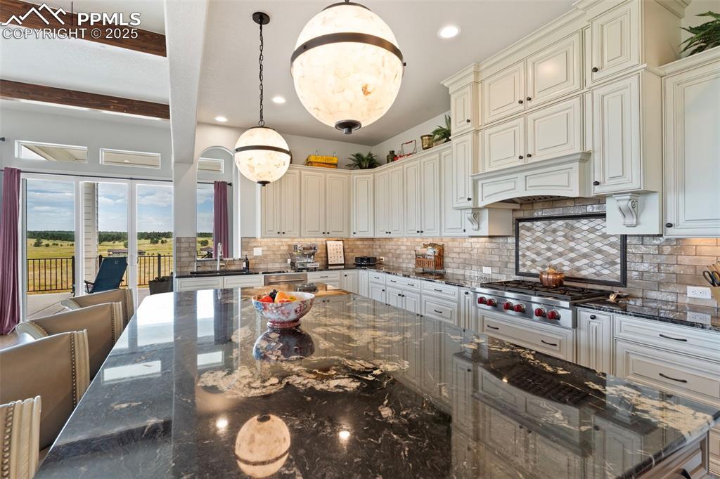 Image 21 of 50: Kitchen featuring dark stone counters, decorative light fixtures, decorativ