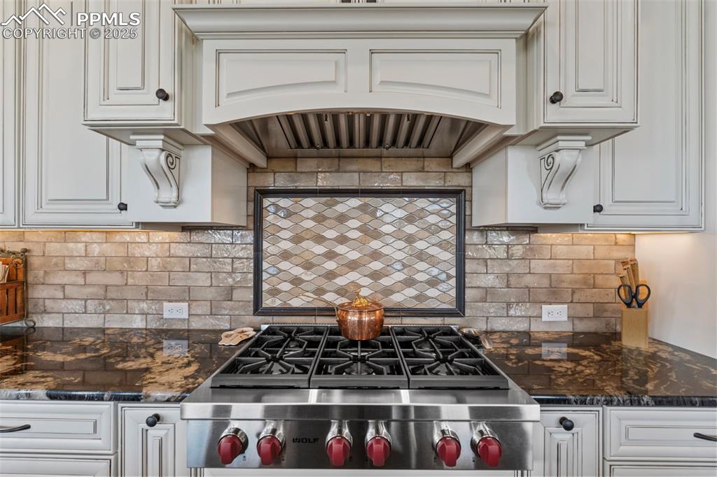 Image 23 of 50: Kitchen with dark stone counters, decorative backsplash, and white cabinetr