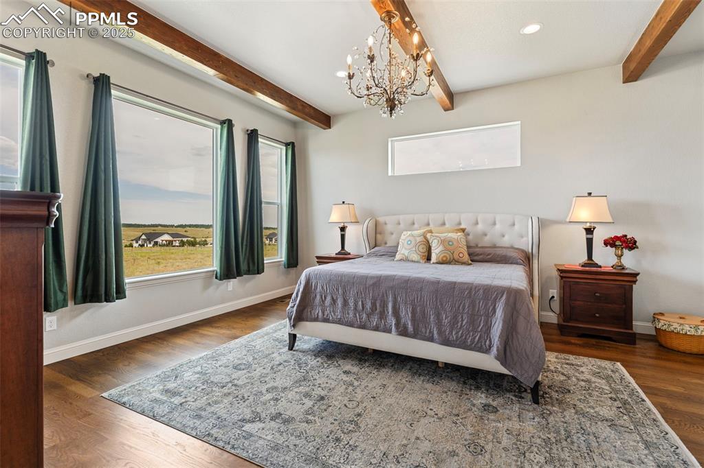 Image 27 of 50: Bedroom featuring beam ceiling, dark wood-style floors, a chandelier, and r