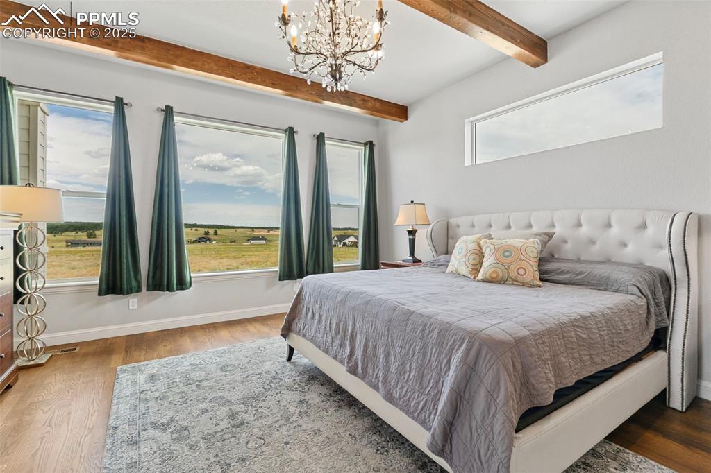 Image 28 of 50: Bedroom with wood finished floors, beam ceiling, and a chandelier