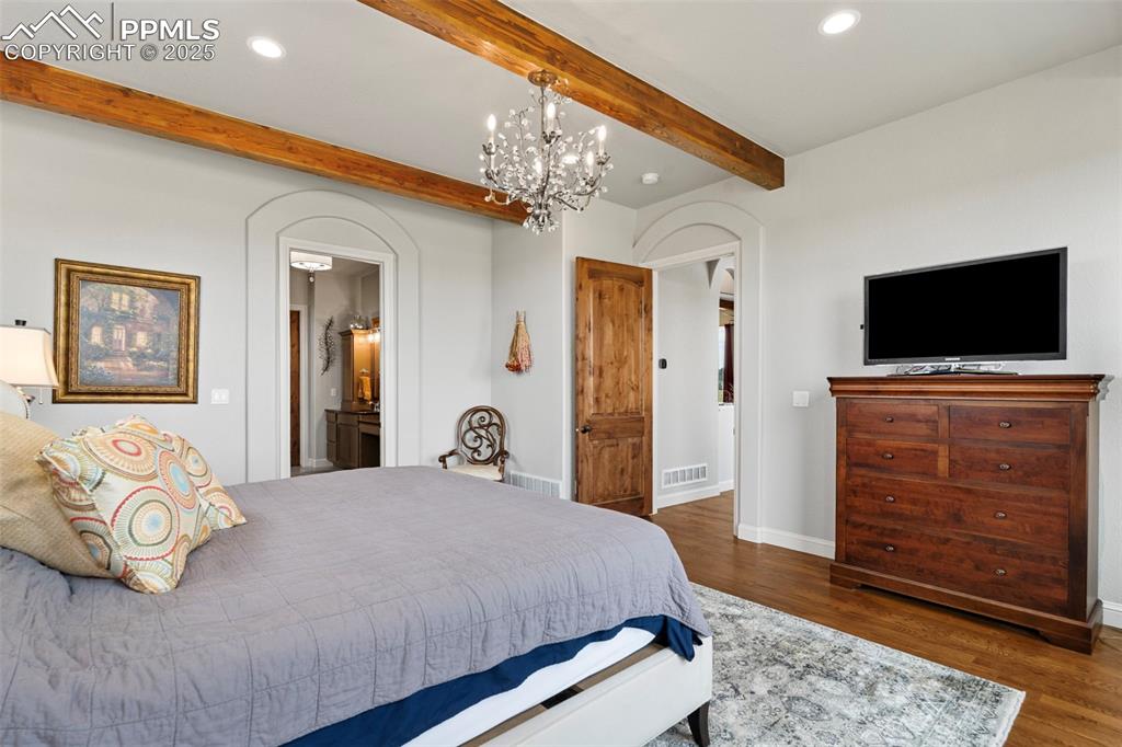 Image 31 of 50: Bedroom with dark wood-style flooring, beamed ceiling, a chandelier, recess