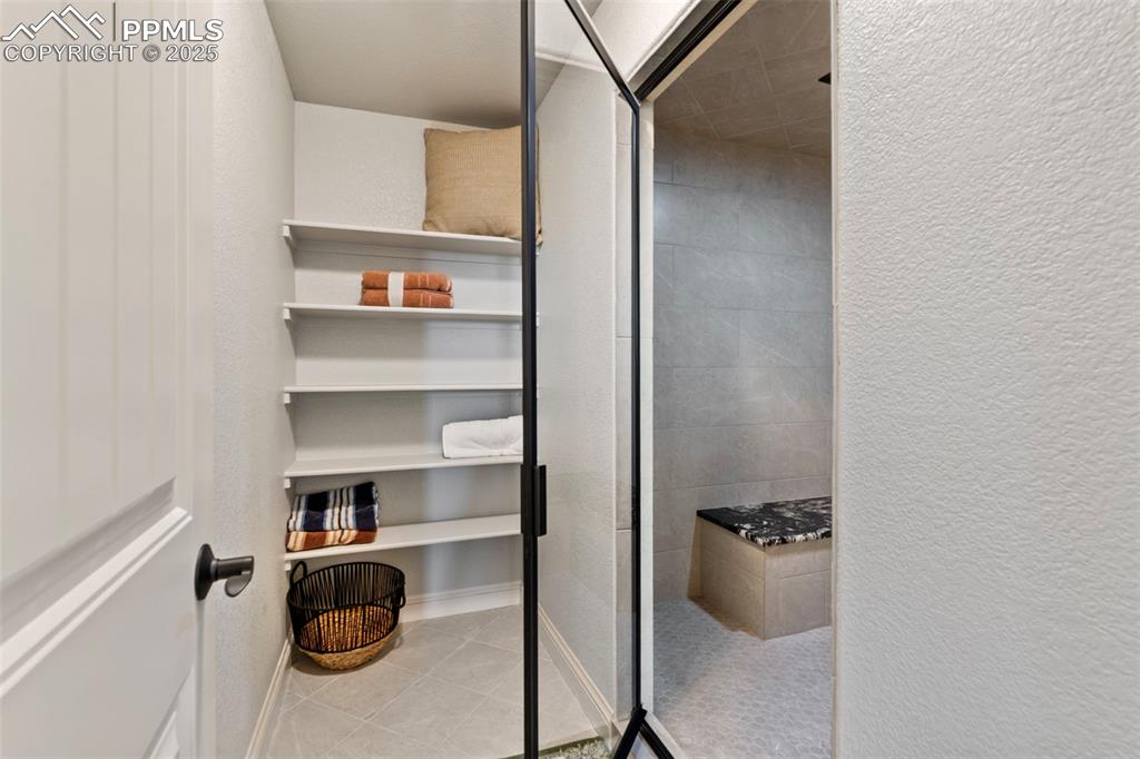 Image 41 of 50: Bathroom with a textured wall, light tile patterned floors, and a stall sho