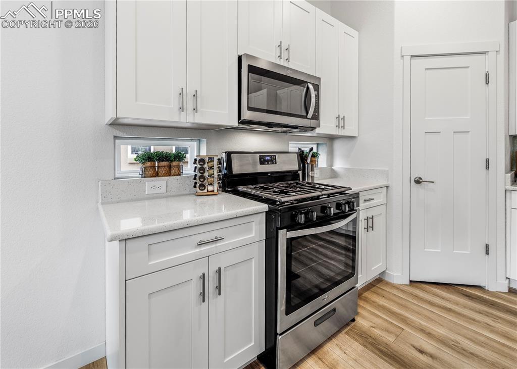 Image 12 of 46: Kitchen with stainless steel appliances, white cabinetry, light wood finish