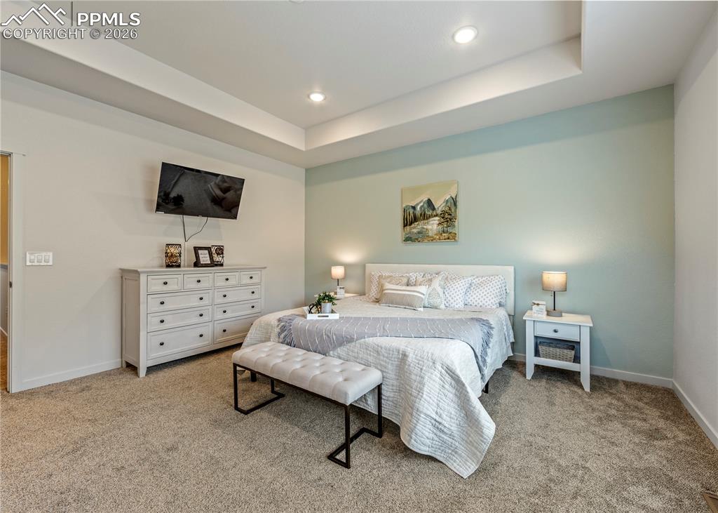 Image 24 of 46: Bedroom featuring light colored carpet, recessed lighting, and a raised cei