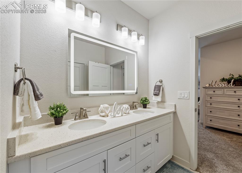 Image 29 of 46: Full bathroom with double vanity, a textured wall, and dark carpet