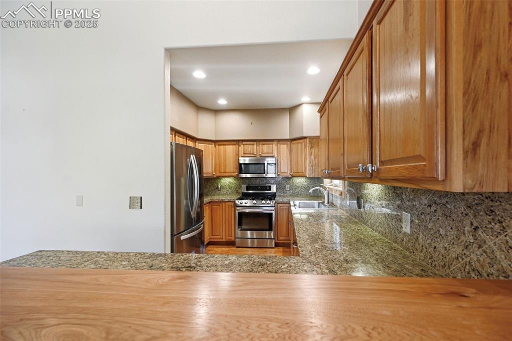 Image 17 of 42: Kitchen with appliances with stainless steel finishes, backsplash, brown ca