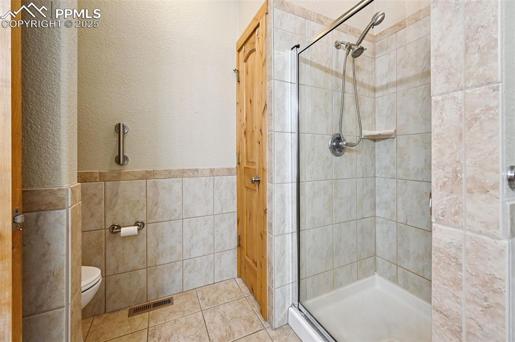 Image 27 of 42: Full bath with a stall shower, tile walls, a textured wall, tile patterned 