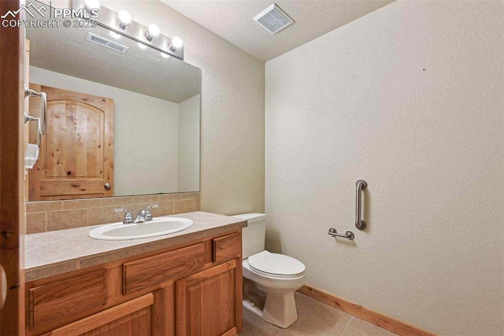 Image 8 of 42: Half bath with a textured wall, vanity, light tile patterned floors, tastef