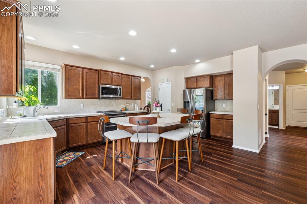 Image 10 of 46: Kitchen with arched walkways, dark wood-style flooring, light countertops,