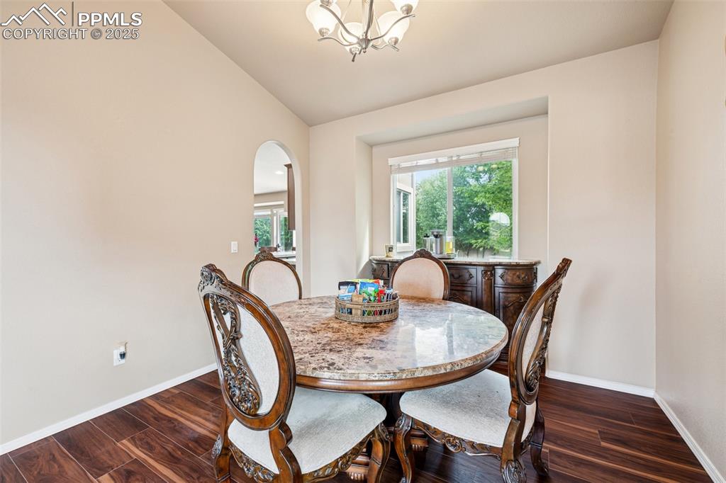 Image 16 of 46: Dining room with dark wood-style floors, lofted ceiling, and arched walkway