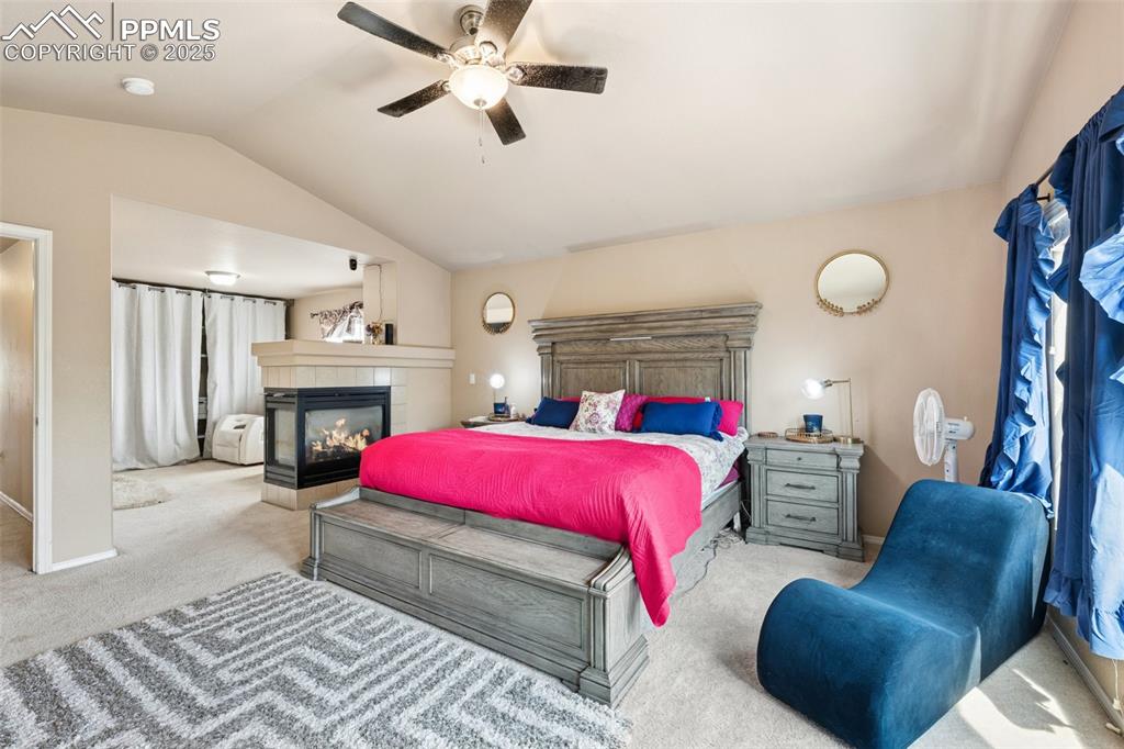 Image 23 of 46: Carpeted bedroom featuring lofted ceiling, a fireplace, and a ceiling fan