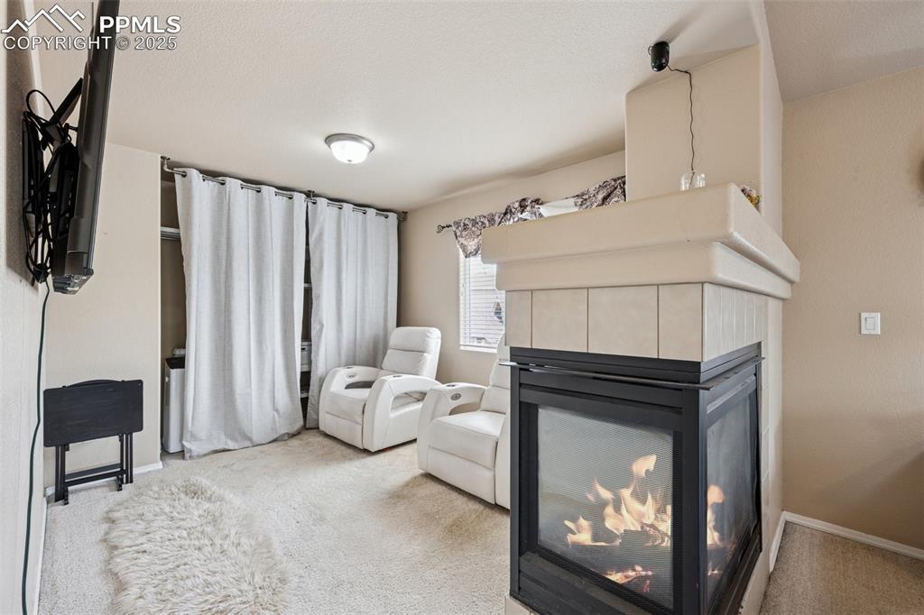 Image 24 of 46: Carpeted sitting area in primary suite featuring a gas fireplace
