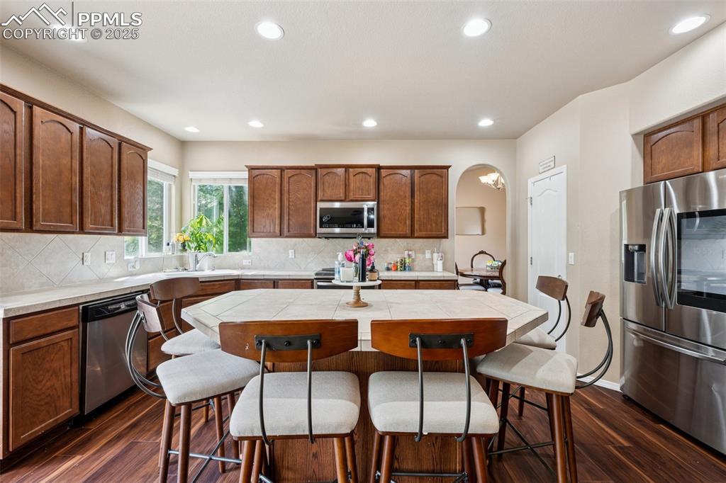 Image 8 of 46: Kitchen with arched walkways, stainless steel appliances, tile counters, a