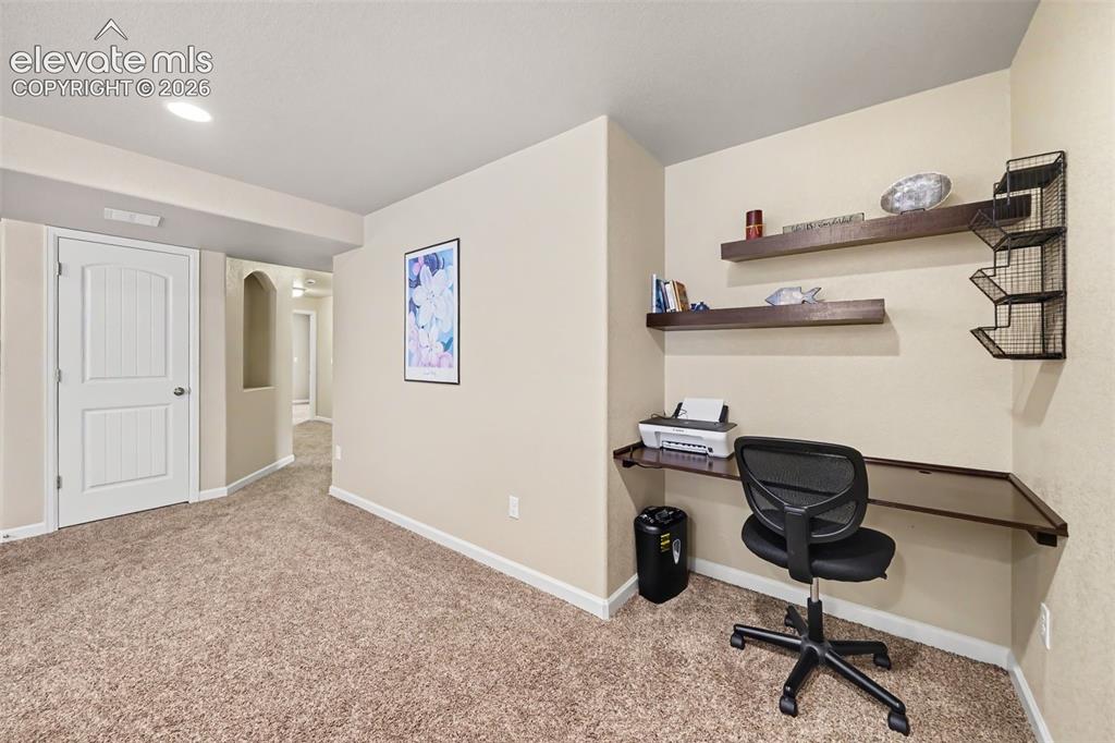 Image 19 of 32: Cozy basement family room featuring built-in shelving and a dedicated desk 
