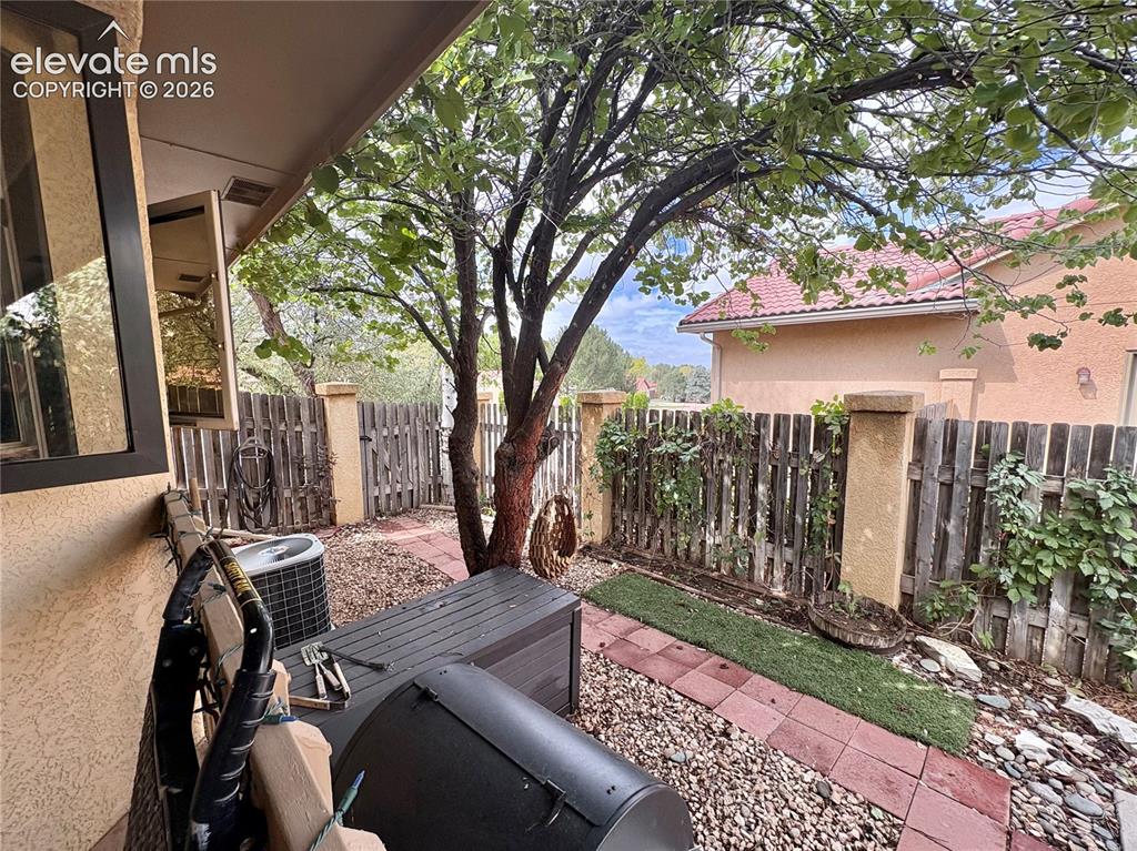 Image 26 of 28: Covered patio space featuring a mature tree, privacy fencing, and a gravel