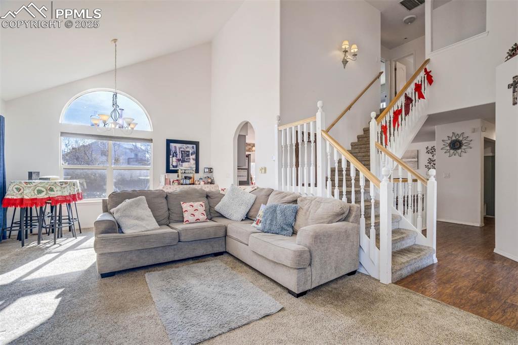 Image 10 of 27: Living area featuring high vaulted ceiling, stairs, carpet, a chandelier, a
